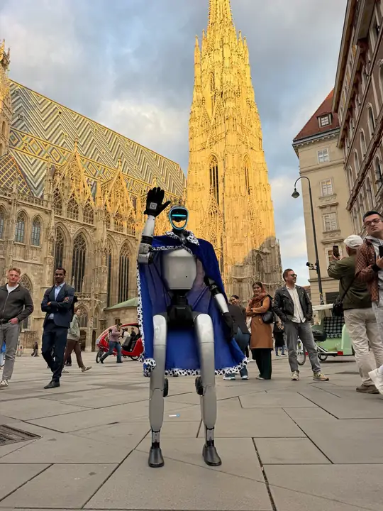 Humanoider Roboter mit blauem Umhang winkt vor dem Wiener Stephansdom, Passanten schauen zu